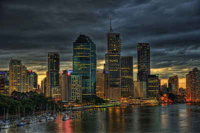 River by modern buildings against sky at dusk