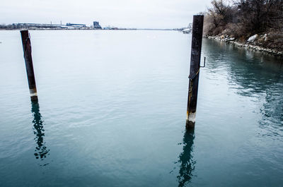 Wooden posts in lake against sky