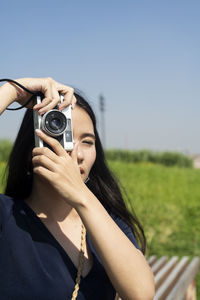 Close-up of woman photographing with camera against clear sky