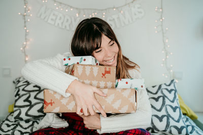 Smiling woman holding christmas gift while sitting on sofa at home
