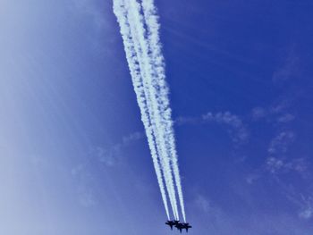 Low angle view of vapor trails against blue sky