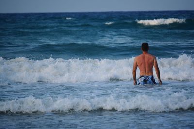 Rear view of shirtless man in sea against sky