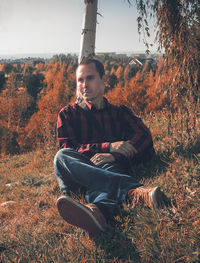 Man sitting against tree trunk at field