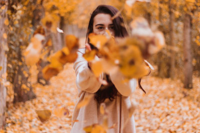 Portrait of young woman playing with autumn leaves