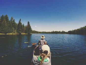 Rear view of people rowing boat in river against clear blue sky