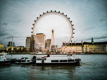 Ferris wheel in city against cloudy sky