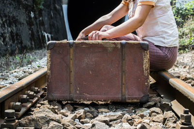 Low section of woman with suitcase sitting on railroad track