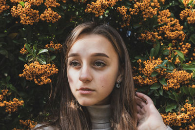 Close-up of thoughtful young woman standing against orange berries on plant