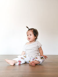 Cute baby girl lying on floor against wall