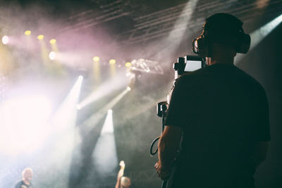 Rear view of cameraman standing against illuminated stage at concert