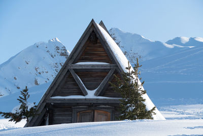 Snow covered house by mountain against sky