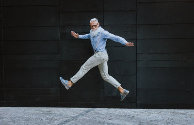 Senior hipster jumping against wall