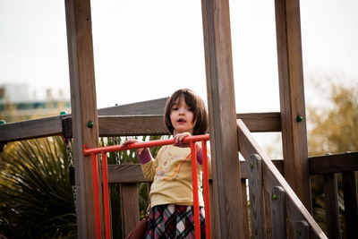 Portrait of happy girl standing on railing against sky