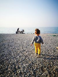 Rear view of a toddler girl on beach against clear sky