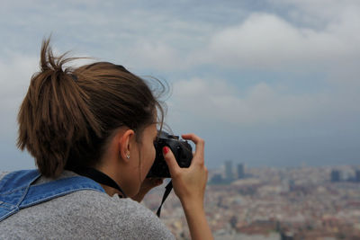 Rear view of woman photographing against cloudy sky