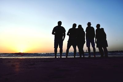 Silhouette people on beach against sky during sunset