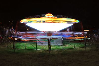 Illuminated carousel at amusement park against sky at night