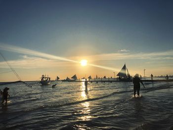 Silhouette people on sea against sky during sunset