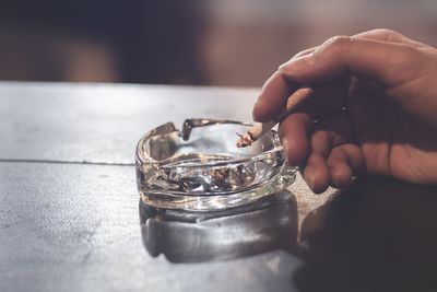 Close-up of person holding cigarette in ashtray on table