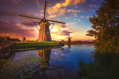Traditional windmill by water against sky during sunset