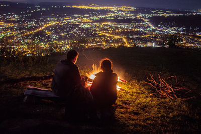 Rear view of couple sitting by bonfire at night