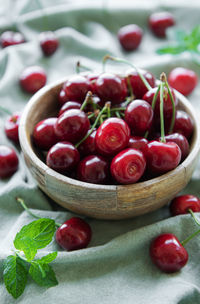 Fresh red cherries fruit in bowl on a green textile background