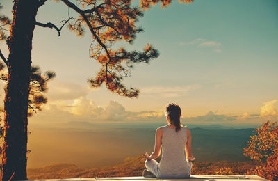 Rear view of woman practicing yoga against cloudy sky during sunset