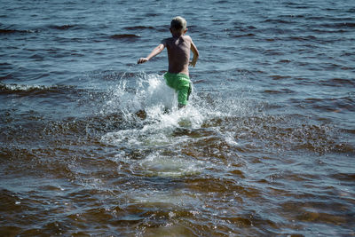 Full length of boy splashing water in sea