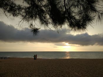 People standing on beach against sky during sunset