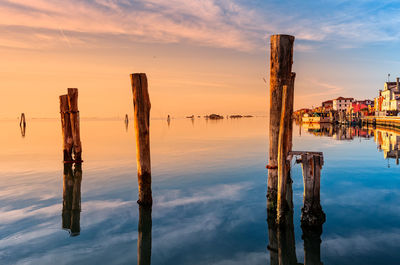 Wooden posts on sea against sky during sunset