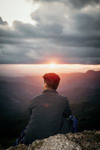 Rear view of man sitting on rock against sky