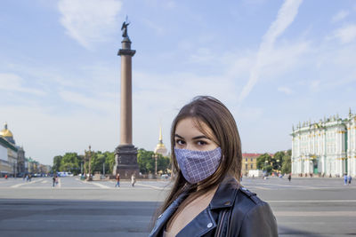 Portrait beautiful young woman in medical mask on palace square in st. petersburg. positive fashion