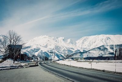 Road by snowcapped mountains against sky during winter