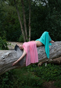 Full length of woman lying down on tree trunk in forest