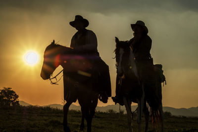 Men riding horses on field against sky during sunset