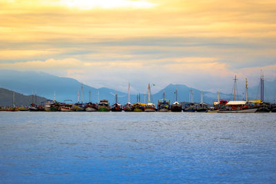 Sailboats moored on sea against mountains and sky during sunset