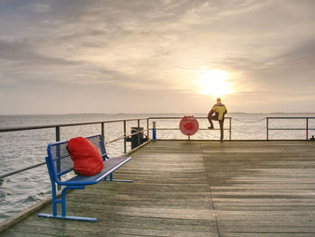 Deck chairs on beach against sky during sunset