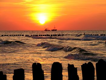 Silhouette boats sailing on sea against orange sky