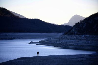 Silhouette person standing on shore against sky