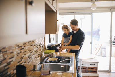 Father making coffee while carrying daughter at home