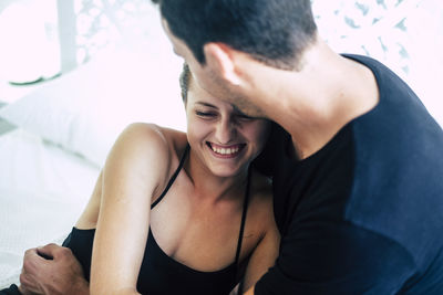 Young man embracing woman while sitting on bed at home