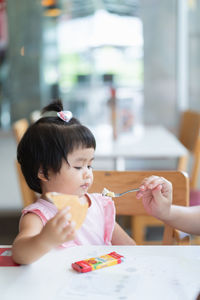 Cropped hand of woman feeding baby girl at home