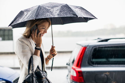 Businesswoman talking on smart phone during rainy season in city