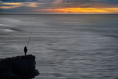 Silhouette of an angler standing on a rock. sunset