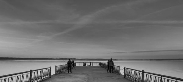 People on pier in lake against sky