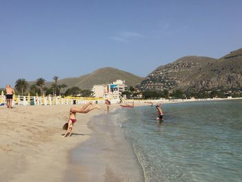 People on beach against clear blue sky