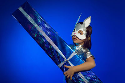 Christmas baby boy in hare mask with gift in studio on blue wall background