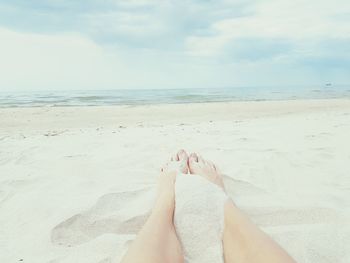 Low section of person relaxing on beach against sky