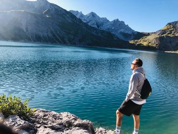 Rear view of man standing by lake against mountains