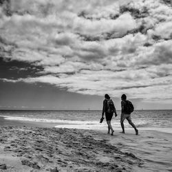 Rear view of people on beach against cloudy sky